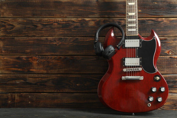 Beautiful six - string electric guitar with headphones against wooden background, space for text