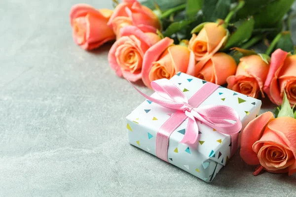 Φρέσκα πορτοκαλί τριαντάφυλλα με δώρο και χώρο για το κείμενο του γκρίζου προγρού — Φωτογραφία Αρχείου