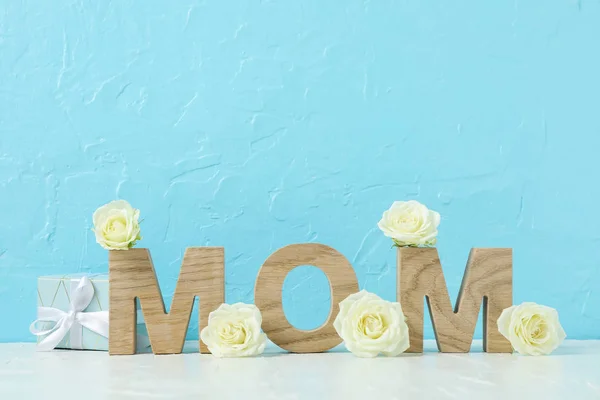 Inschrift Mama mit weißen Rosen auf rosa Tisch gegen Farbe bac — Stockfoto