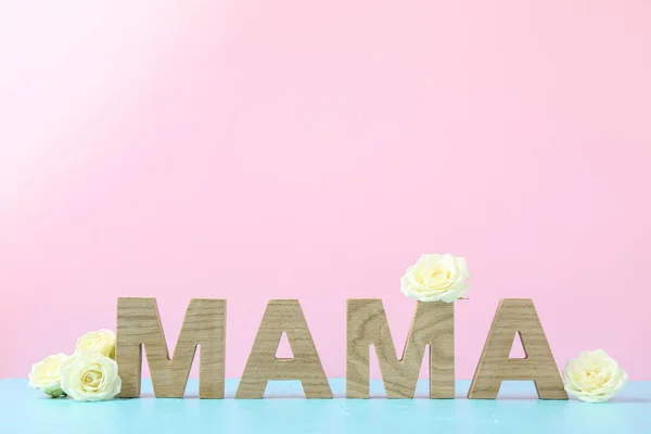 Inschrift Mama mit weißen Rosen auf blauem Tisch gegen Farbe bac — Stockfoto