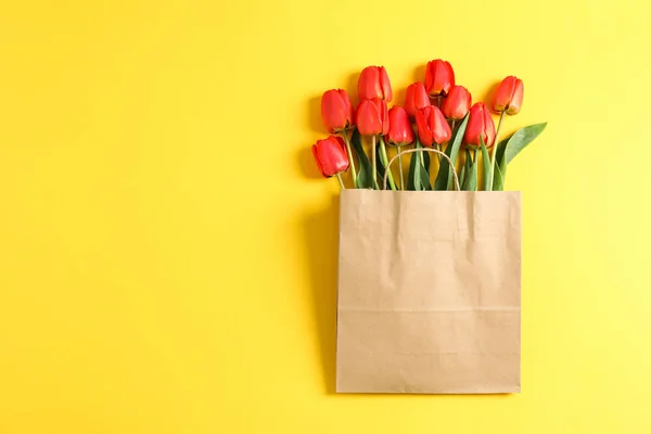 Paper bag with beautiful red tulips on yellow background, space for text