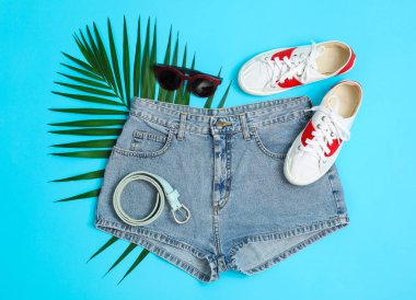 Düz lay kompozisyon: kadın giysi ve aksesuarları, mavi arka plan üzerinde palmiye yaprağı. Yaz arka planı