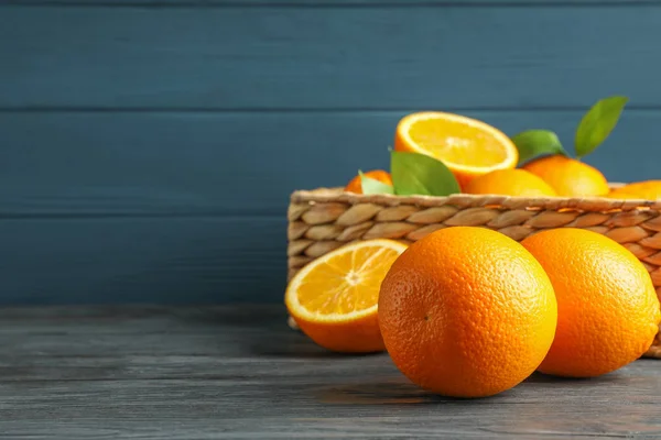 Ψάθινο καλάθι με ώριμα πορτοκάλια σε ξύλινο τραπέζι, χώρος για κείμενο — Φωτογραφία Αρχείου