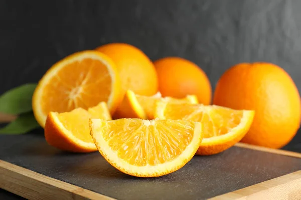 Schneidebrett mit orangefarbenen Stücken vor schwarzem Hintergrund, schließen — Stockfoto