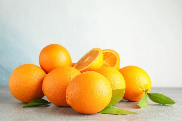 Ώριμα πορτοκάλια με φύλλα σε γκρίζο τραπέζι με ανοιχτόχρωμο φόντο, — Φωτογραφία Αρχείου