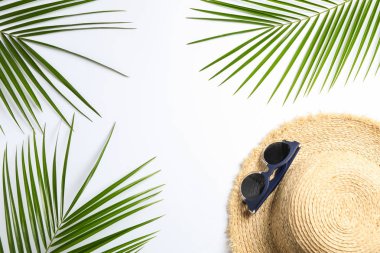 Beyaz üzerinde hasır şapka, güneş gözlüğü ve palmiye yaprakları ile kompozisyon 