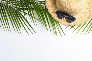 Beyaz üzerinde hasır şapka, güneş gözlüğü ve palmiye yaprakları ile kompozisyon 