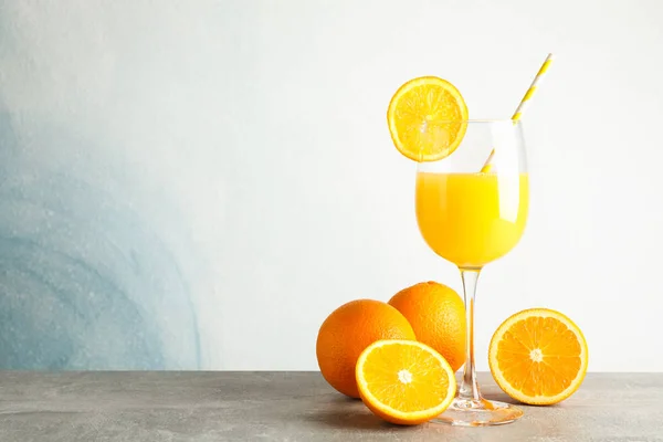 Glass with fresh orange juice and tubule, oranges on grey table — Stock Photo, Image