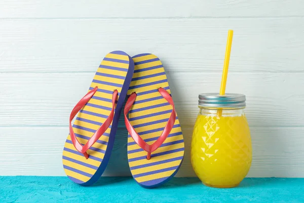 Chinelos e jarro de vidro com suco fresco na tabela de cores contra — Fotografia de Stock