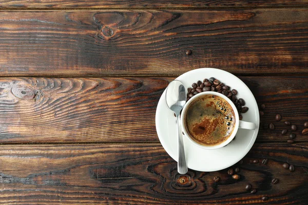 Cup of coffee with spoon and coffee beans on wooden background,