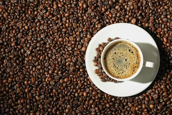 Tazza di caffè con schiuma schiumosa su sfondo fagioli, vista dall'alto e — Foto Stock