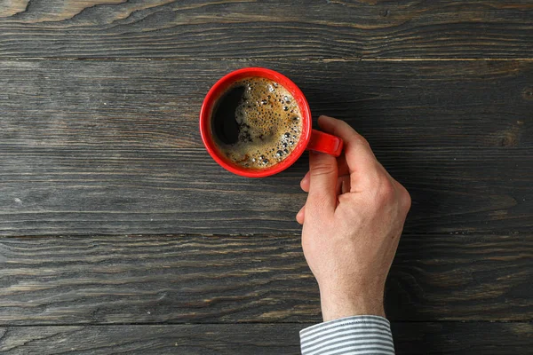 Ruka, která drží šálek kávy s pěnou pěny na dřevěné backgrounu — Stock fotografie