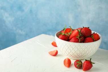Mavi backgro karşı beyaz masada taze çilek ile Bowl