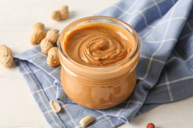 Beyaz üzerinde fıstık ezmesi, fıstık ve mutfak havlusu ile cam kavanoz 