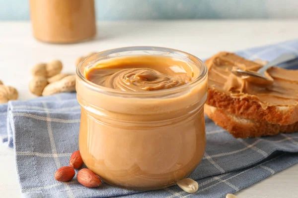Glass jar with peanut butter, peanut, kitchen towel, spoon and p