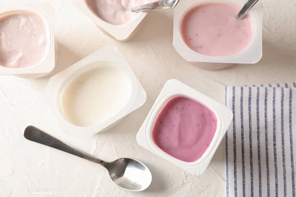Komposition mit Plastikbechern mit Joghurt auf weißem Tisch — Stockfoto