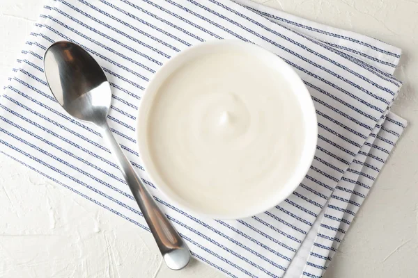 ถ้วยโยเกิร์ตครีมเปรี้ยว ช้อนและผ้าเช็ดตัวบนหลังซีเมนต์สีขาว — ภาพถ่ายสต็อก