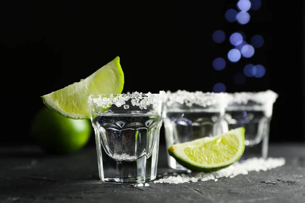 Tiros de tequila con rodajas de sal y lima sobre fondo negro — Foto de Stock