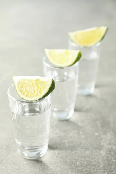 Tequila tiros com fatias de limão no fundo cinza — Fotografia de Stock