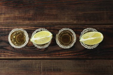 Ahşap masada tuz ve kireç dilimleri ile tekila çekim, üst görünümü