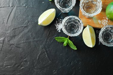 Siyah masa üzerinde tuz, limon dilimleri ve nane ile tekila çekim