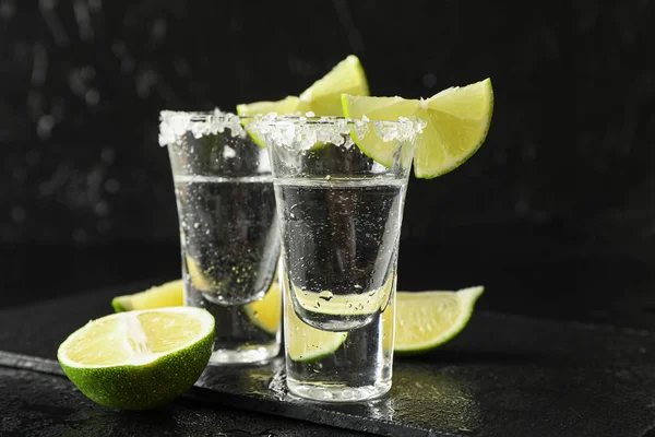 Tequila shots avec des tranches de sel et de citron vert sur fond noir humide — Photo