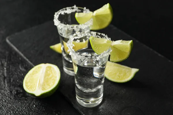 Tiros de tequila con rodajas de sal y lima sobre fondo negro húmedo —  Fotos de Stock
