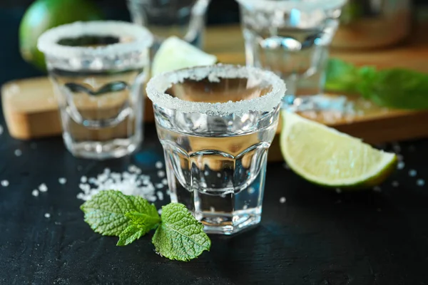 Tequila tiros com sal, fatias de limão e hortelã na mesa preta — Fotografia de Stock