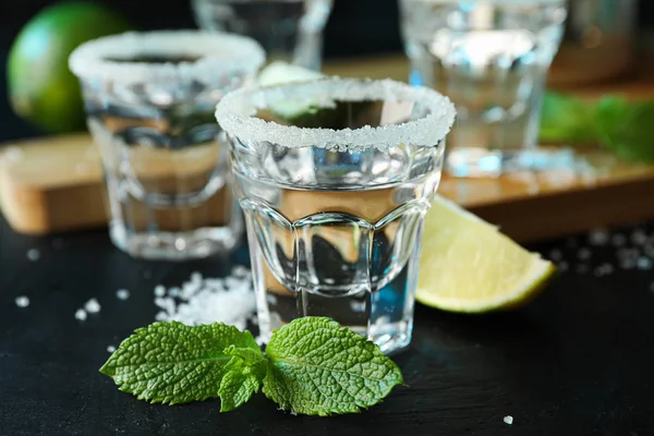 Tequila tiros com sal, fatias de limão e hortelã na mesa preta — Fotografia de Stock