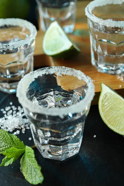 Tequila tiros com sal, fatias de limão e hortelã na mesa preta — Fotografia de Stock