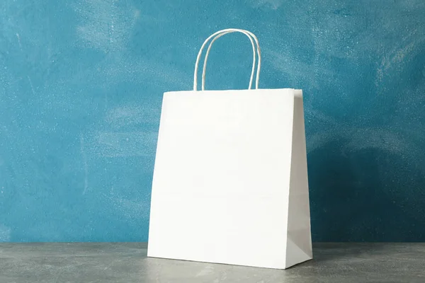 White paper bag on grey table against blue background, copy spac — Stock Photo, Image