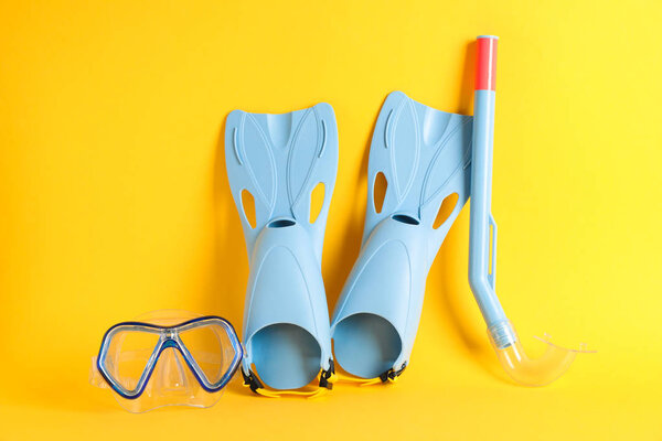 Flippers, snorkel and diving mask on yellow background, space fo