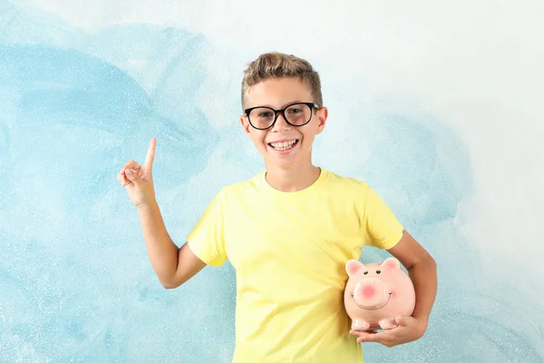 Boy in glasses with piggy bank against color background, space f — Stock Photo, Image