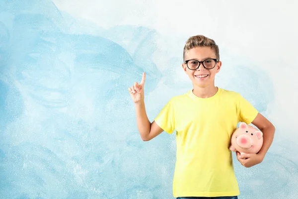 Boy in glasses with piggy bank against color background, space f — Stock Photo, Image