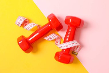 İki tonlu arka planda dumbbells ve ölçme bandı, kopya alanı