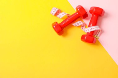 İki tonlu arka planda dumbbells ve ölçme bandı, kopya alanı