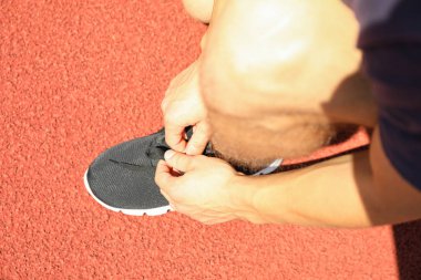 Kırmızı atletik koşu pistinde ayakkabı bağcıkları bağlayan adam, yakın