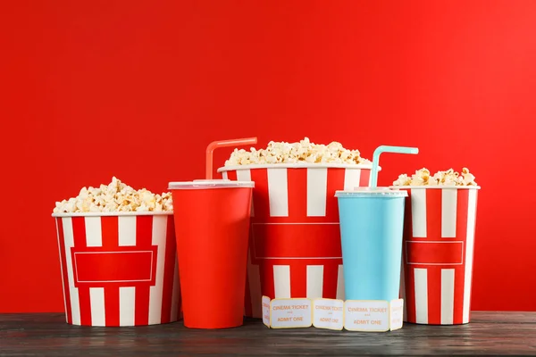 Popcorn buckets, paper cups and tickets against red background, — Stock Photo, Image