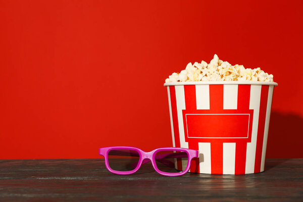 3d glasses and striped bucket with popcorn against red backgroun
