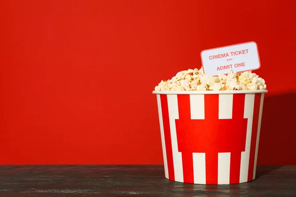 Randig skopa med popcorn och biljetter mot röd bakgrund — Stockfoto