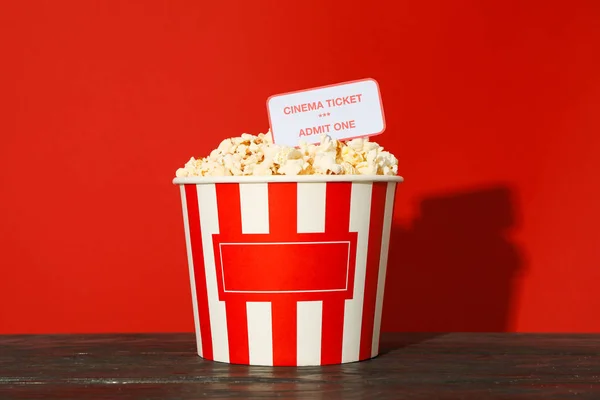 Striped bucket with popcorn and tickets against red background — Stock Photo, Image