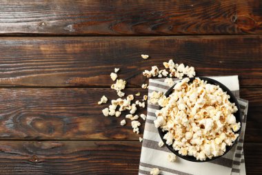 Towel and bowl with popcorn on wooden background, copy space clipart