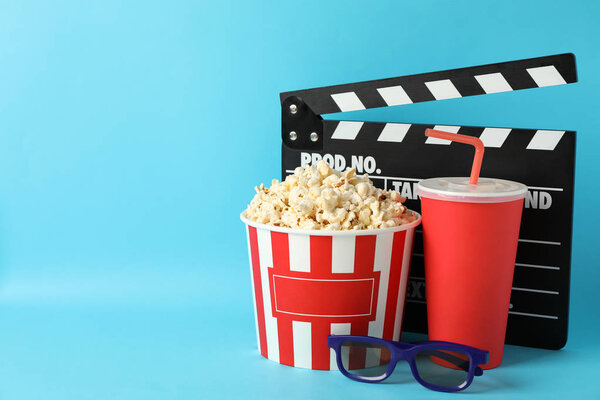 Clapperboard, bucket with popcorn, drink and 3d glasses on blue 