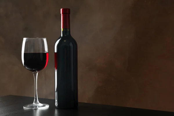Бутылка и стакан с вином на коричневом фоне, пространство для копирования — стоковое фото
