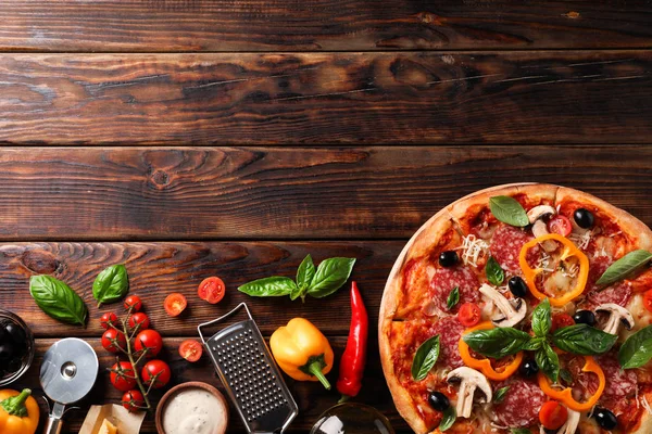 Deliciosa pizza e ingredientes sobre fondo de madera, espacio para copiar — Foto de Stock
