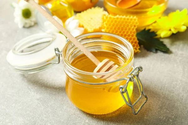 Frasco de vidro com mel, dipper, favos de mel e flores em bac cinza — Fotografia de Stock