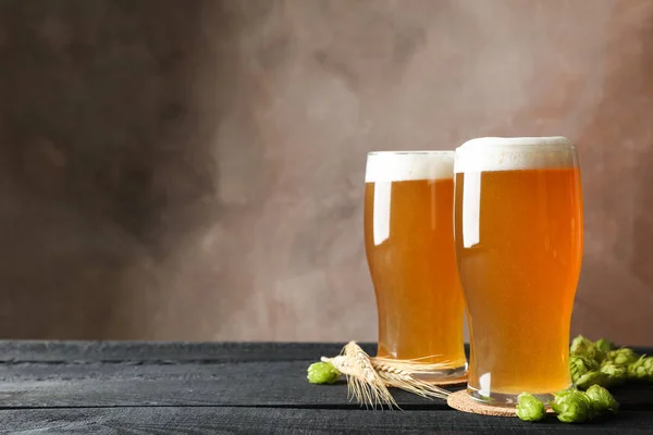 Glasses with beer, hop cones and spikelets on wooden table, spac — Stock Photo, Image