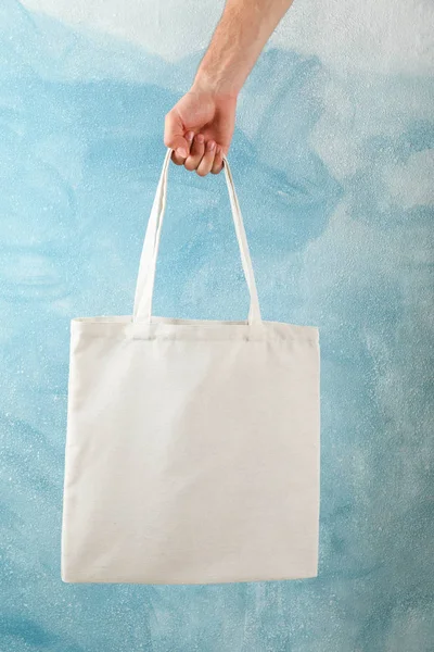 Male hand holding tote bag against blue background, copy space — Stock Photo, Image