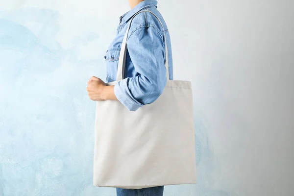 Young woman holding tote bag against blue background, empty spac