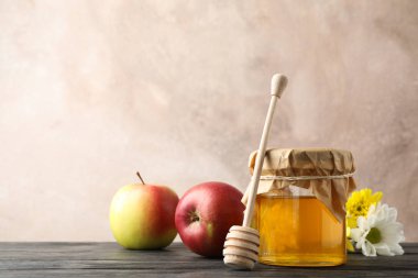 Glass jar with honey, dipper, apples and flowers on wooden backg